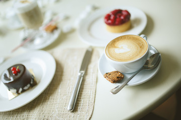 cup of cappuccino and cakes on table