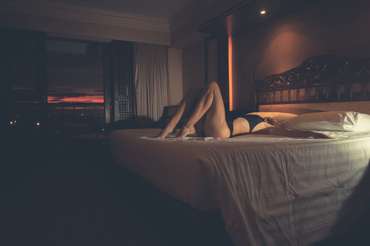 Sexy woman on bed in hotel at sunset