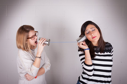 Blonde and brunette women talking with tin can telephone