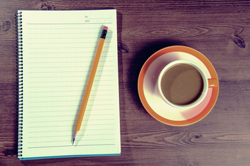 Cup of coffee and notebook on a wooden with vintage colour.