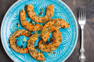 Roasted pumpkin slices with herbs on wooden table in a blue bowl
