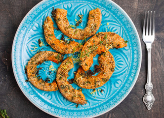 Roasted pumpkin slices with herbs on wooden table in a blue bowl