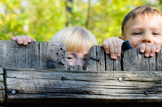 Two children peeking over a wooden fence