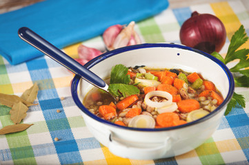Vegetable soup in a metal bowl on a rural rustic wooden table.