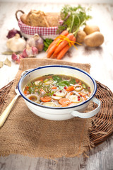 Vegetable soup in a metal bowl on a rural rustic wooden table.