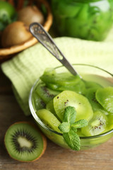 Tasty kiwi jam in glass bowl and jar on wooden background
