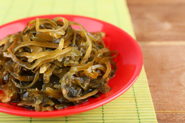 Seaweed in red plat on bamboo mat and wooden table background