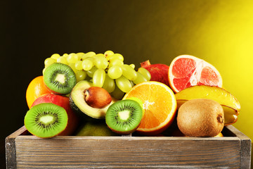 Assortment of fruits in box on dark yellow background