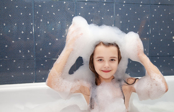 little girl sitting in a bath with soap suds on her head