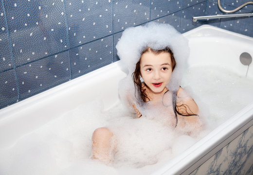 surprised little girl sitting in a bath with soap suds