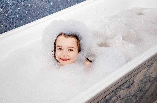 little girl lying in a bath with soap suds