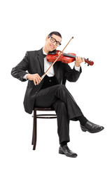 Young violinist playing a violin seated on a chair © Ljupco Smokovski