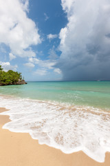Beach on tropical island. Clear blue water, sand, clouds.