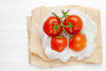 fresh ripe large wet tomatoes in plastic bag on a white wooden b