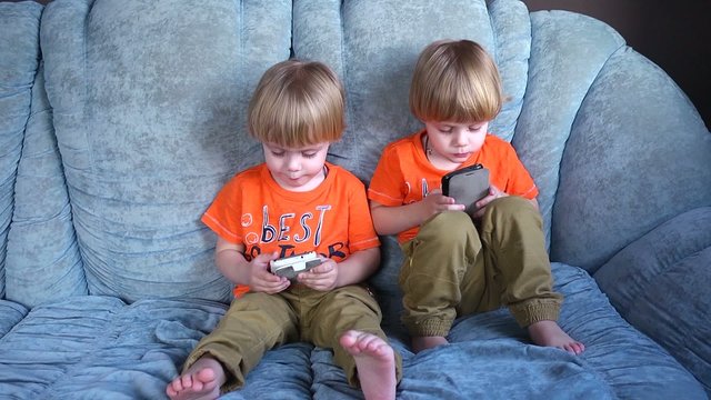 Kids twins having fun playing with mobile cell phones on a couch