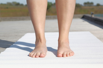 Practicing yoga. Woman standing outside on a mat.