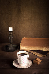 Stack of old books, cup of coffee, candy and candle on the old w