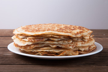 Stack of Russian pancakes - blini on a wite plate on old wooden