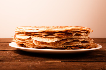 Stack of Russian pancakes - blini on a wite plate on old wooden
