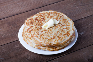 Stack of Russian pancakes - blini on a wite plate on old wooden