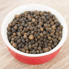 Black Peppercorns - Black peppercorns in a red bowl.
