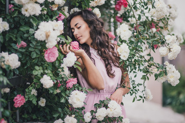 Beautiful young woman in a pink dress posing in a rose garden