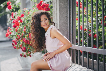 Beautiful young woman in a pink dress posing in a rose garden