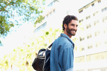 Happy young man traveling with bag outdoors