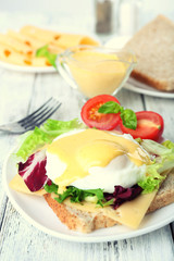 Toast with egg Benedict and tomato on plate on wooden table