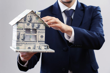 Model of house made of money in male hands on white background