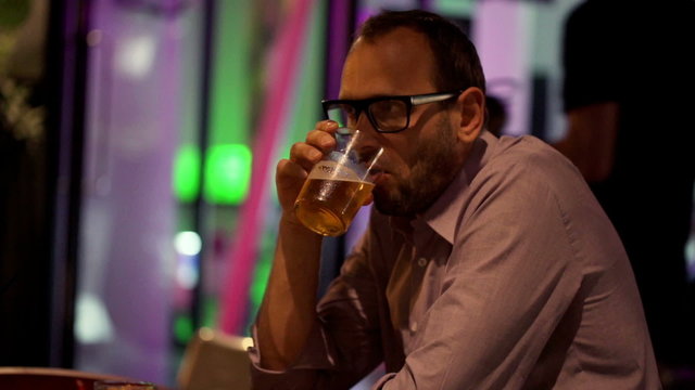 Unhappy, sad man drinking beer sitting in cafe at night