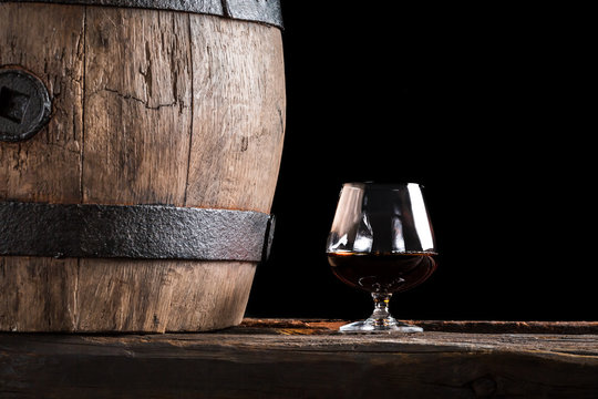 Glass of cognac and old wooden barrel