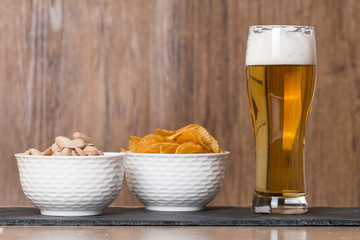 Glass of beer, golden chips and  pistachios in bowl