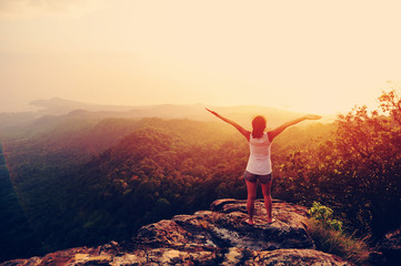 	strong confident woman hiker open arms at on mountain peak rock