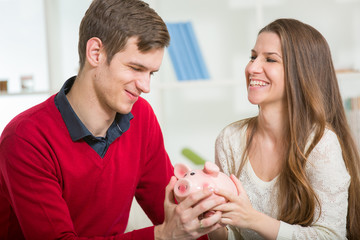 Obraz na płótnie Canvas Young happy couple holding a piggy bank in the living room