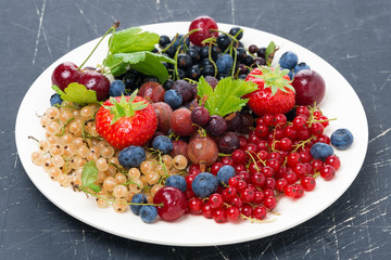 assorted garden berries on a plate on dark background