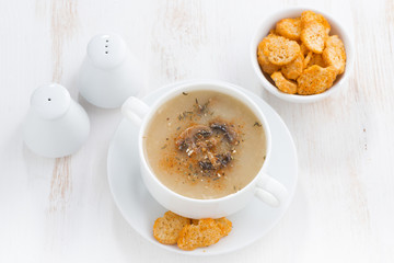 mushroom cream soup with croutons on white table, horizontal