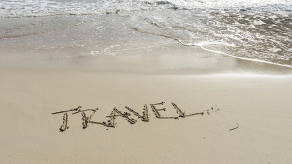 Word travel written on a sandy beach