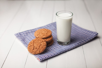 Oatmeal cookies and glass of milk on napkin on white table