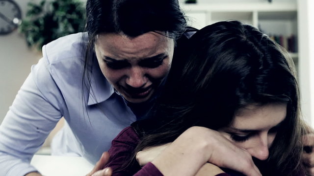 Woman crying hugging teenager daughter