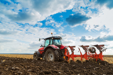 Naklejka premium Farmer plowing stubble field with red tractor
