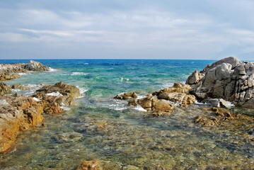 Sunny coastal landscape with rocks, agitated sea and cloudy sky