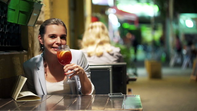 Happy woman raising toast to camera and drinking cocktail