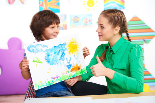 Teacher with thumb up looking at drawing of boy
