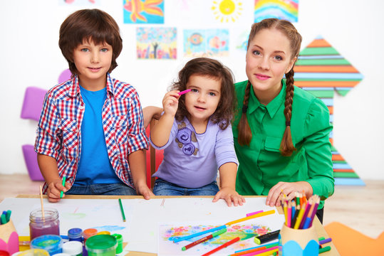 Teacher with children drawing and looking at camera