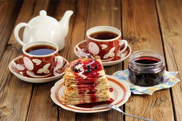 Russian bliny with currant jam, tea cups, pot on wooden backgrou
