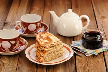 Russian bliny with currant jam, tea cups, pot on wooden backgrou