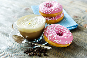 Cup of coffee with pink glazed donuts on wooden background