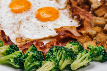 Fried Eggs on a plate with bacon, croutons and broccoli