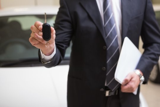 Businessman showing a car key while holding clipboard